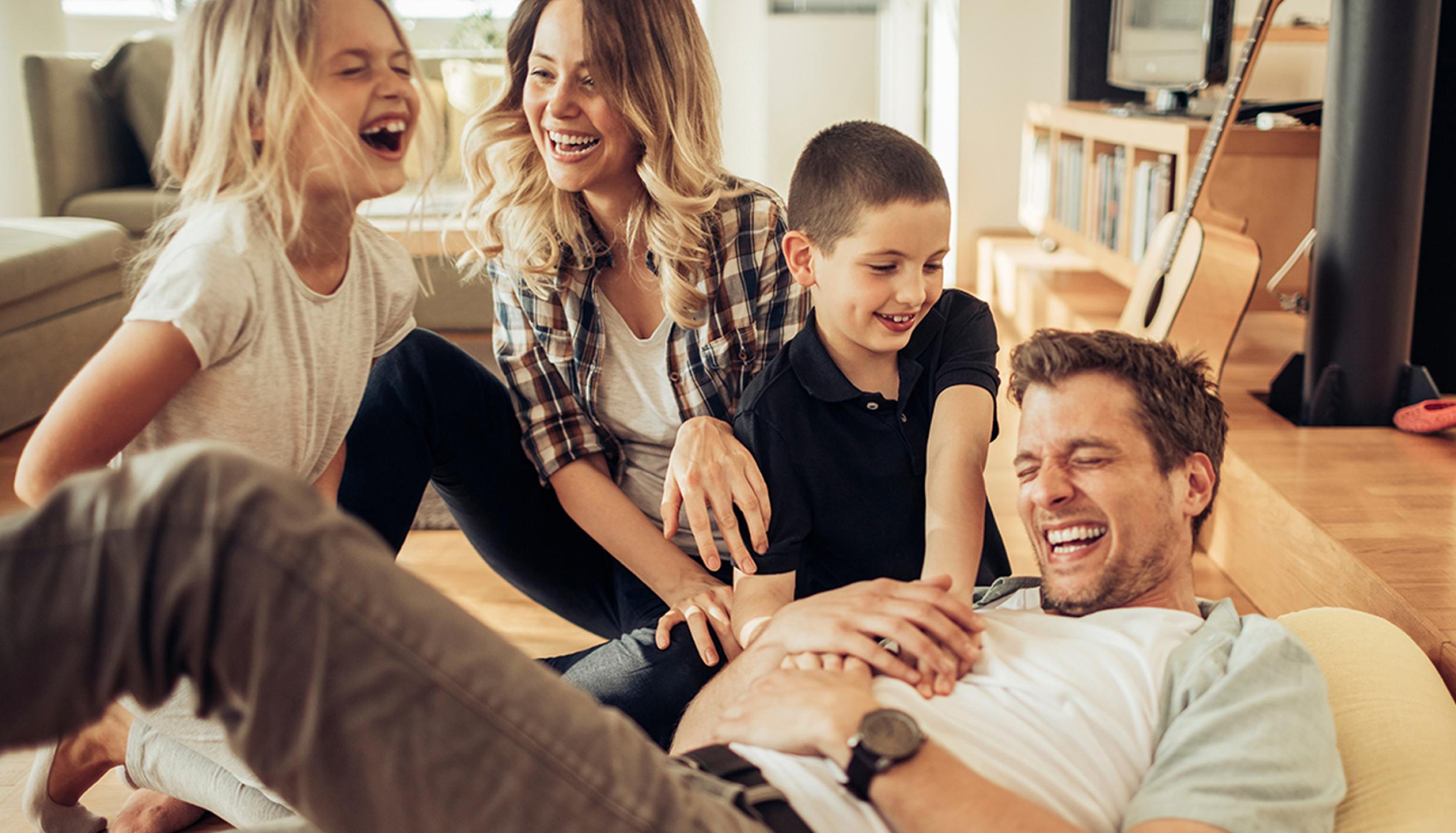 A dad on the couch horsing around with the rest of his family