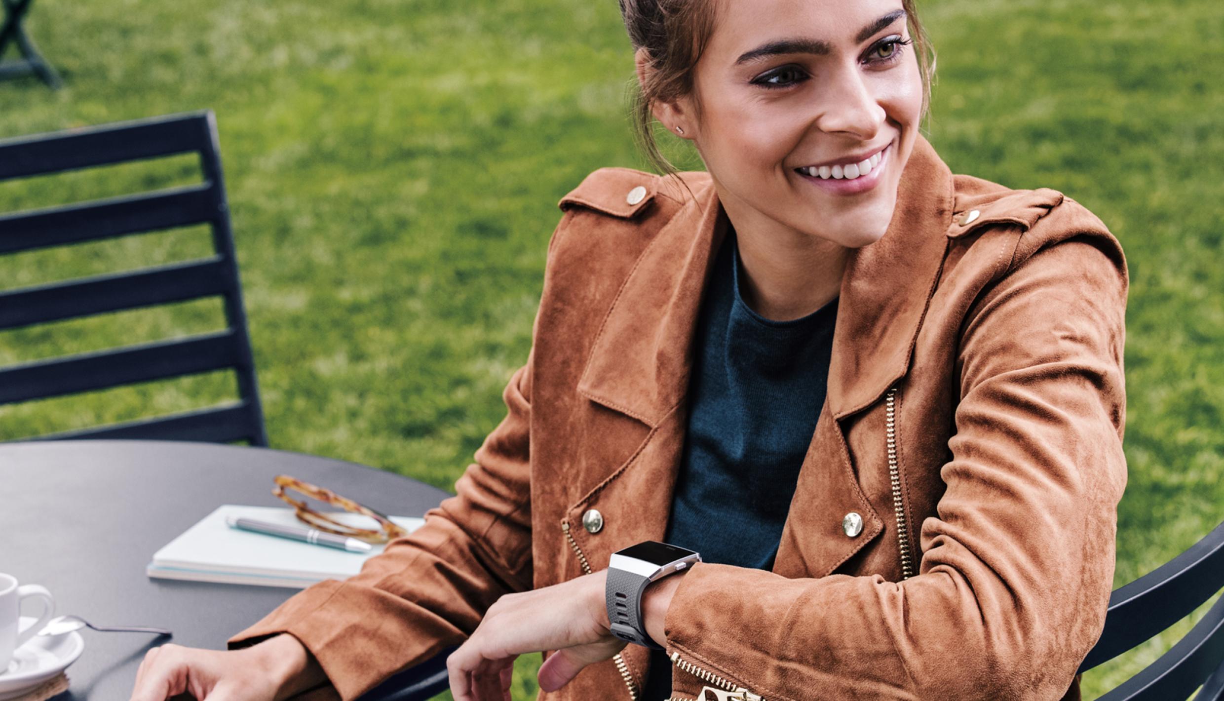 A woman at a cafe table wearing a soft brown leather jacket and with a smart watch on her wrist