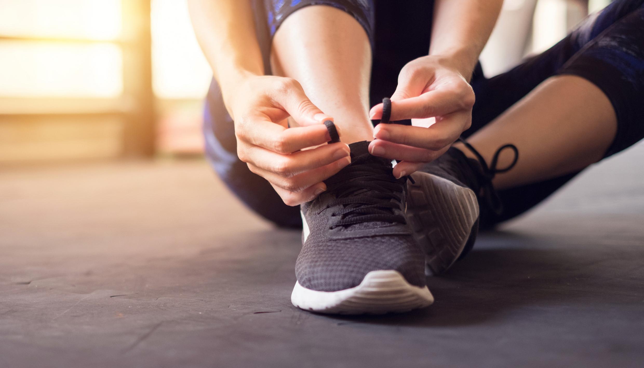 A woman sitting on the floor and tying new running shoes
