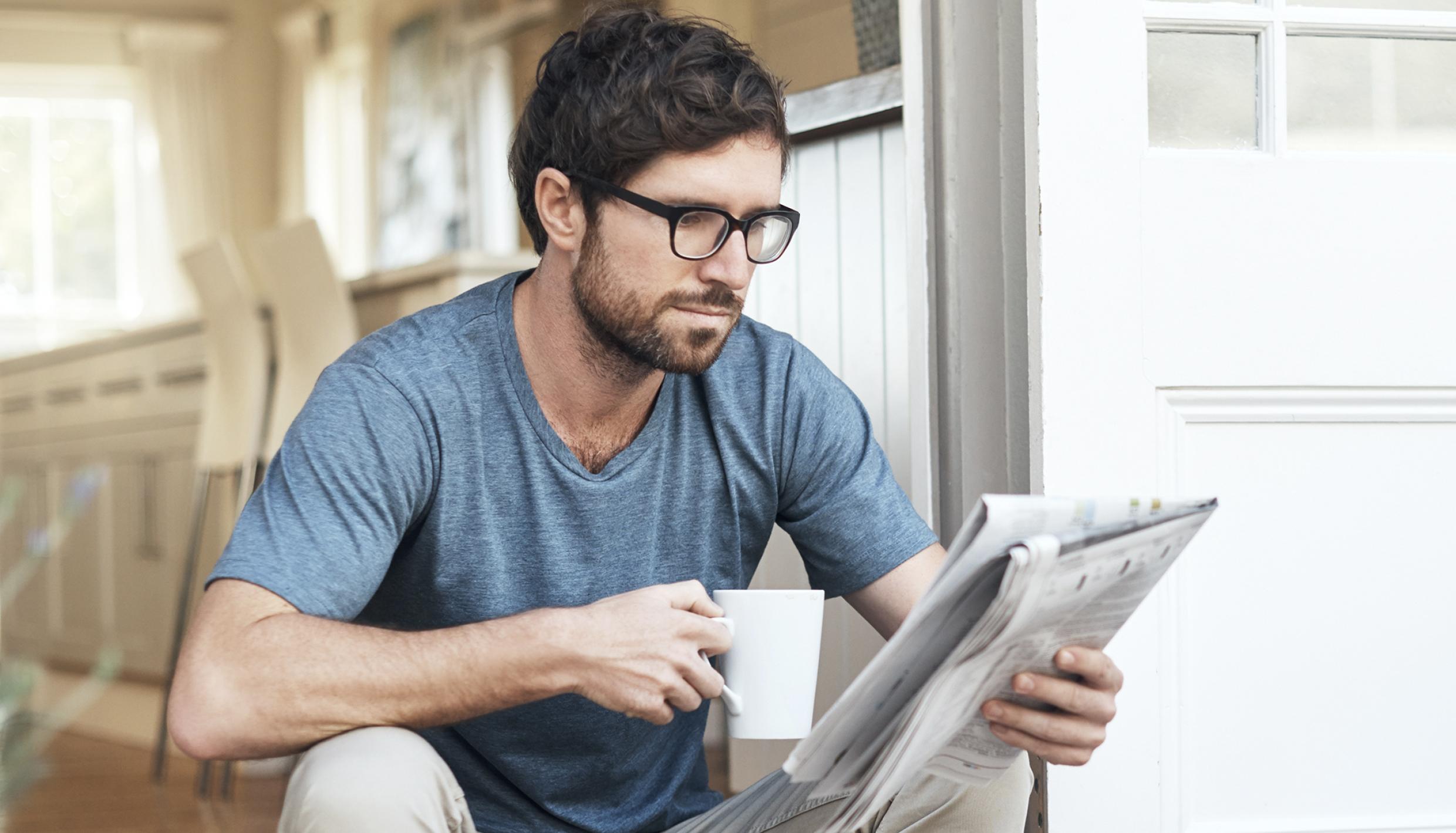 man reading a newspaper on stoop with cup of coffee