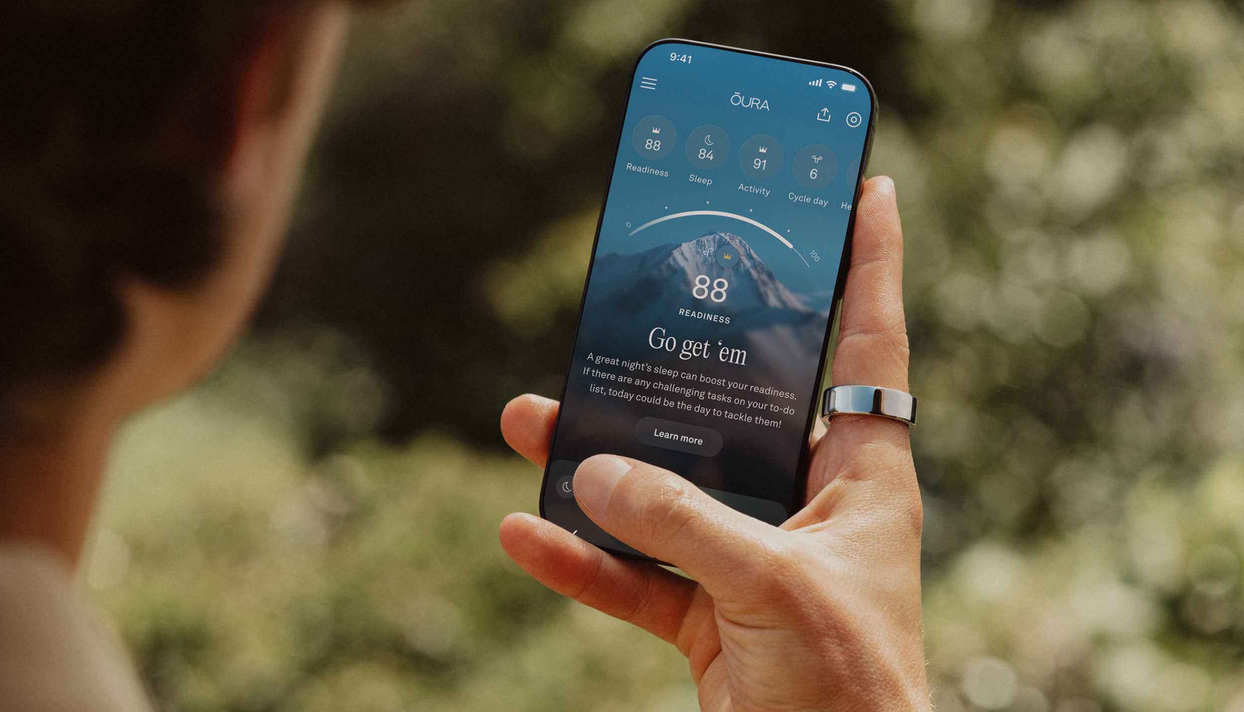 Hombre sosteniendo un teléfono que muestra la aplicación Oura mientras lleva puesto el anillo