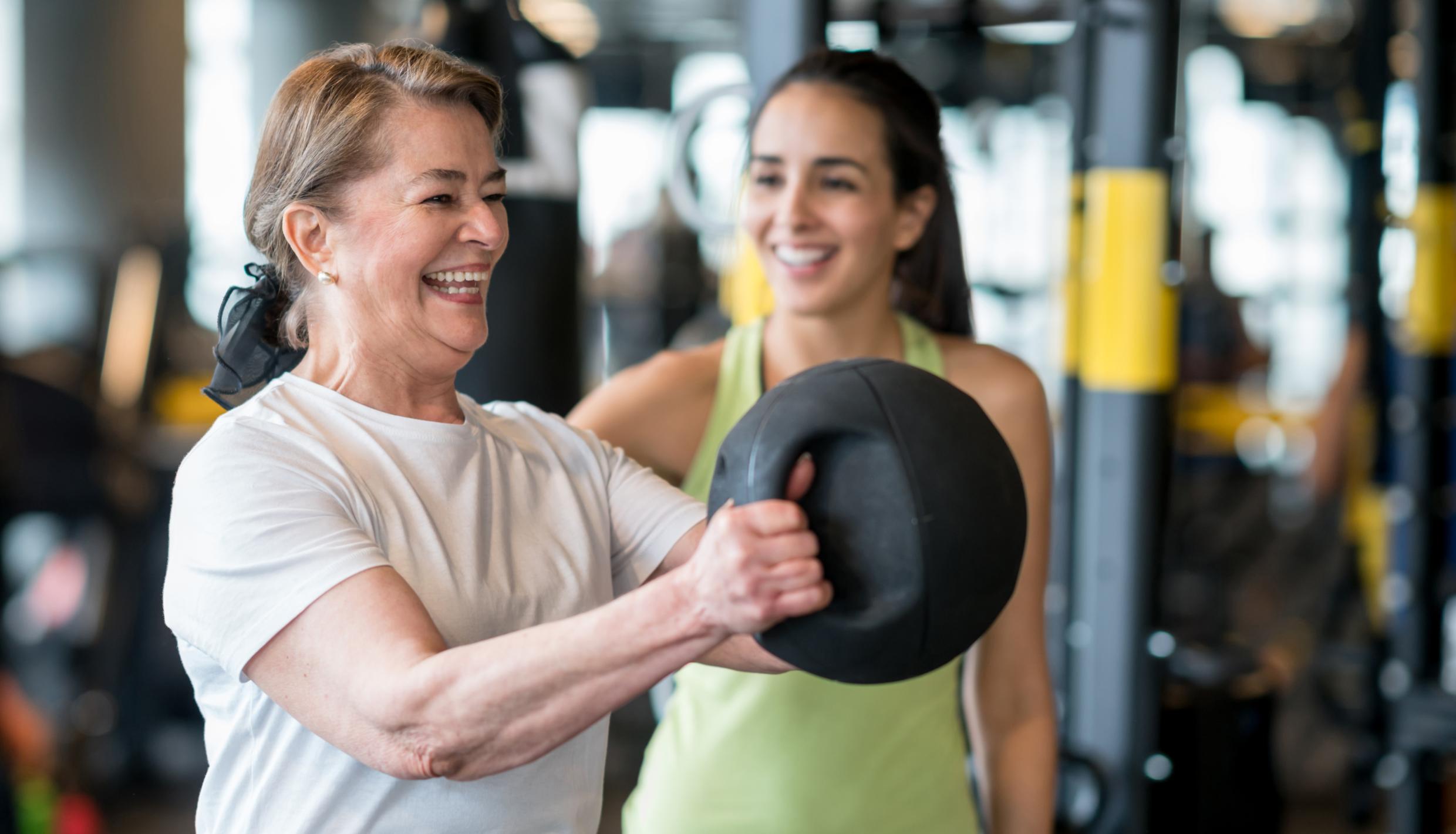 mujer levantando la pelota medicinal con entrenador