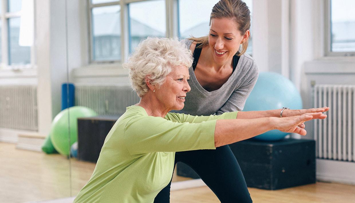 Older woman performing yoga stretches with a young trainer
