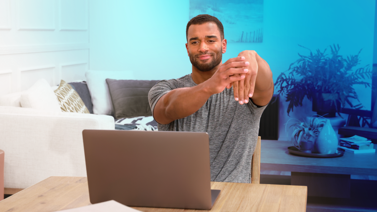 Hombre estirando la muñeca delante de una Computadora portátil
