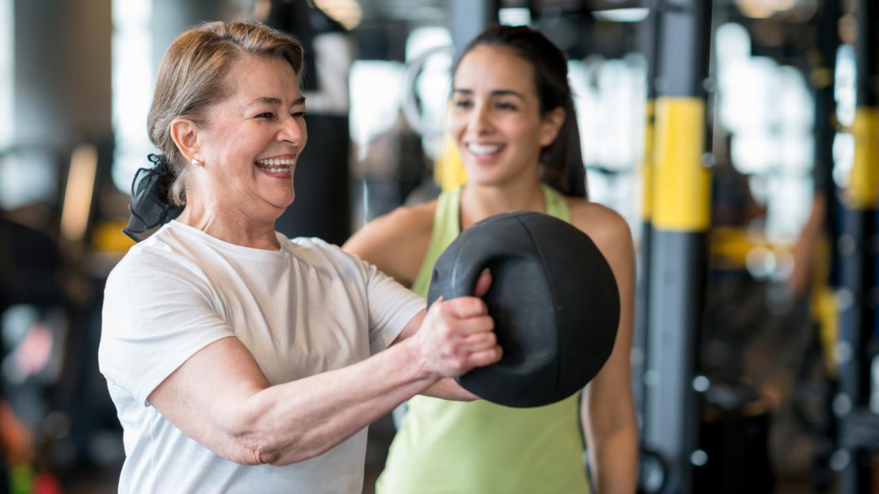 woman lifting medicine ball with trainer