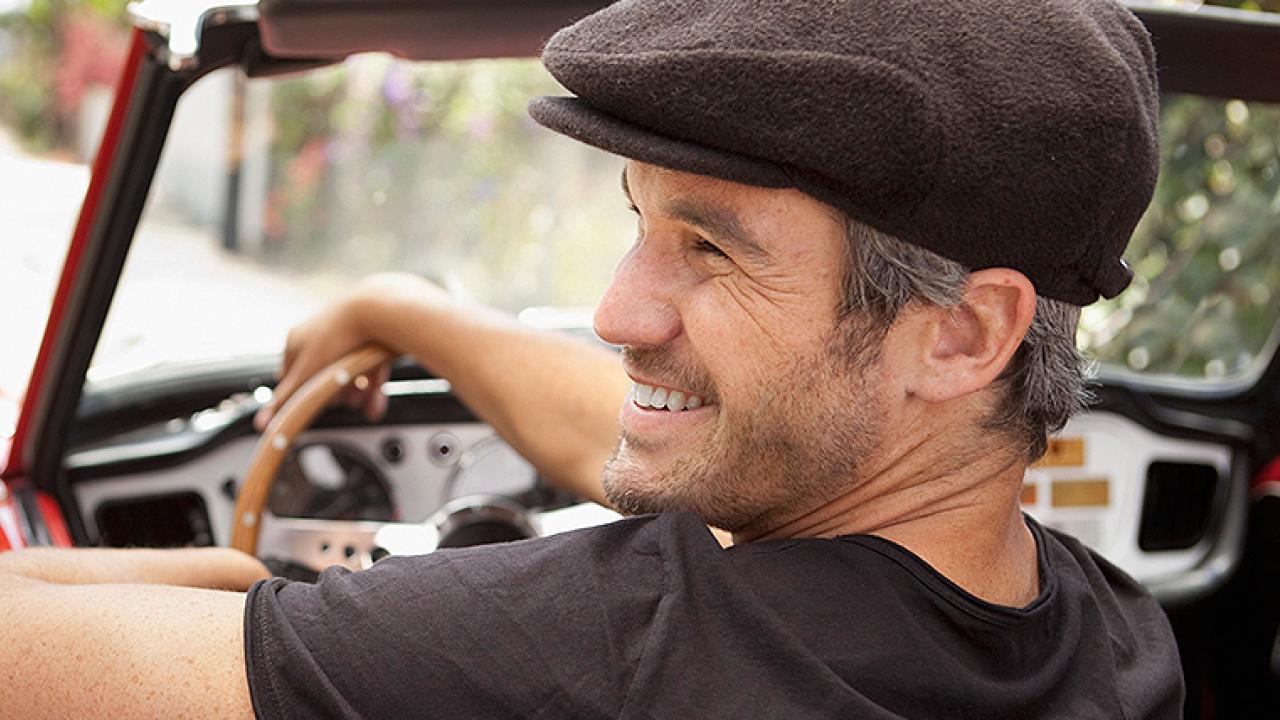 Un chico mayor más fresco en un descapotable rojo con el codo apoyado en la puerta