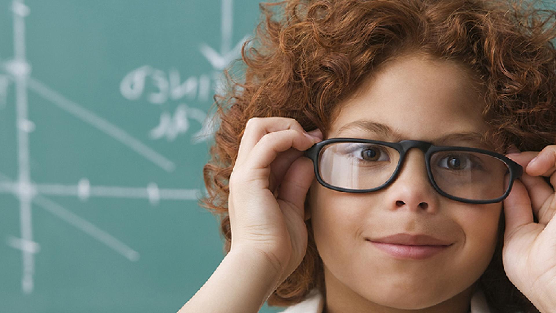 Boy wearing glasses in front of a chalkboard