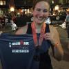 Una mujer sosteniendo una camiseta de Ironman Race Finisher.