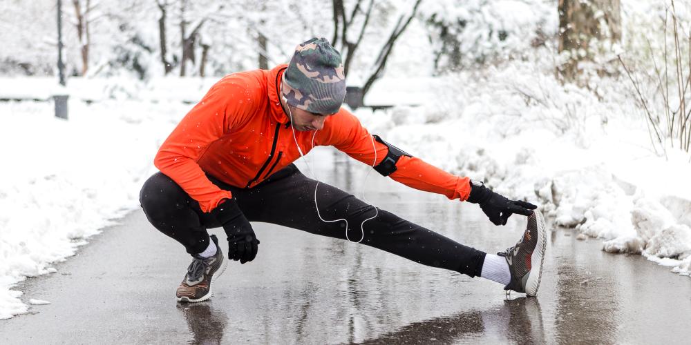 hombre afuera estirando en ropa de entrenamiento de invierno