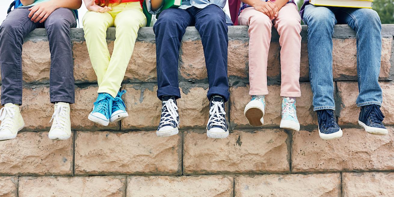 A row of kids dangling their legs over a low wall