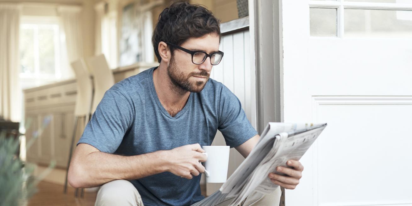 man reading a newspaper on stoop with cup of coffee